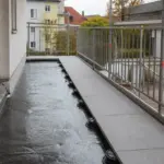 Balkon während der Sanierung mit frisch aufgebrachter schwarzer Abdichtung, verlegten Platten und Metallgeländer
