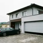 Doppelgarage mit hellem Sektionaltor an einem Einfamilienhaus, davor ein Kombi auf gepflasterter Zufahrt