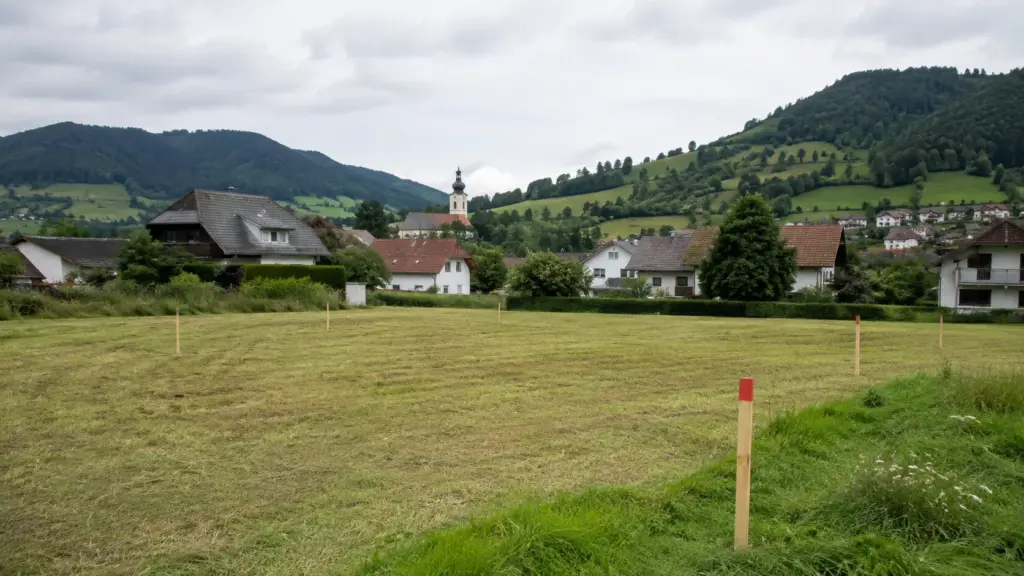 Unbebautes Baugrundstück mit Vermessungspflöcken am Rand eines österreichischen Dorfes