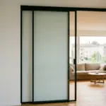Zweiflügelige Glasschiebetür mit schwarzem Rahmen zwischen Flur und Wohnraum