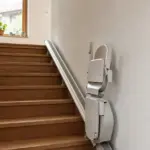 Treppenlift mit hochgeklapptem Sitz an der Schiene einer Holztreppe im Einfamilienhaus